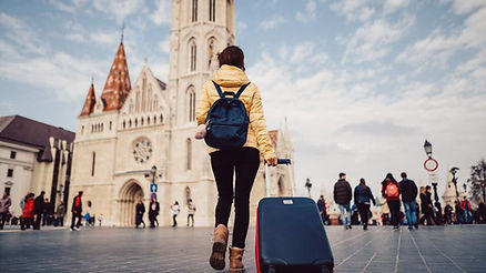 woman in yellow puffer jacket with blue suitcase walking toward cathedral